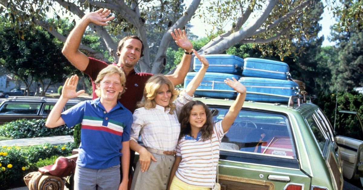 National Lampoon's Family Vacation crew smiles and waves in front of their station wagon.