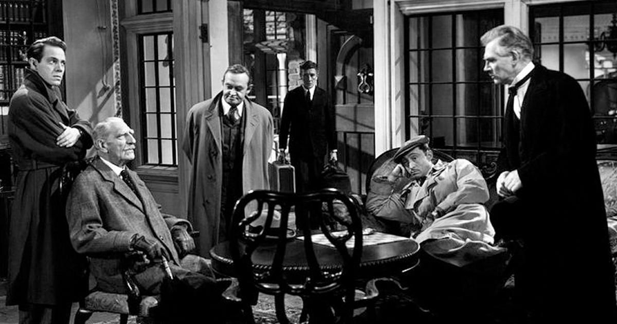 The cast of And Then There Were None, including Barry Fitzgerald as Judge Francis, Walter Huston as Dr. Edward, Louis Hayward as Philip Lombard, Roland Young as Detective William, all in long coats and suits Sitting and standing together in a room and discussing.  Something together.