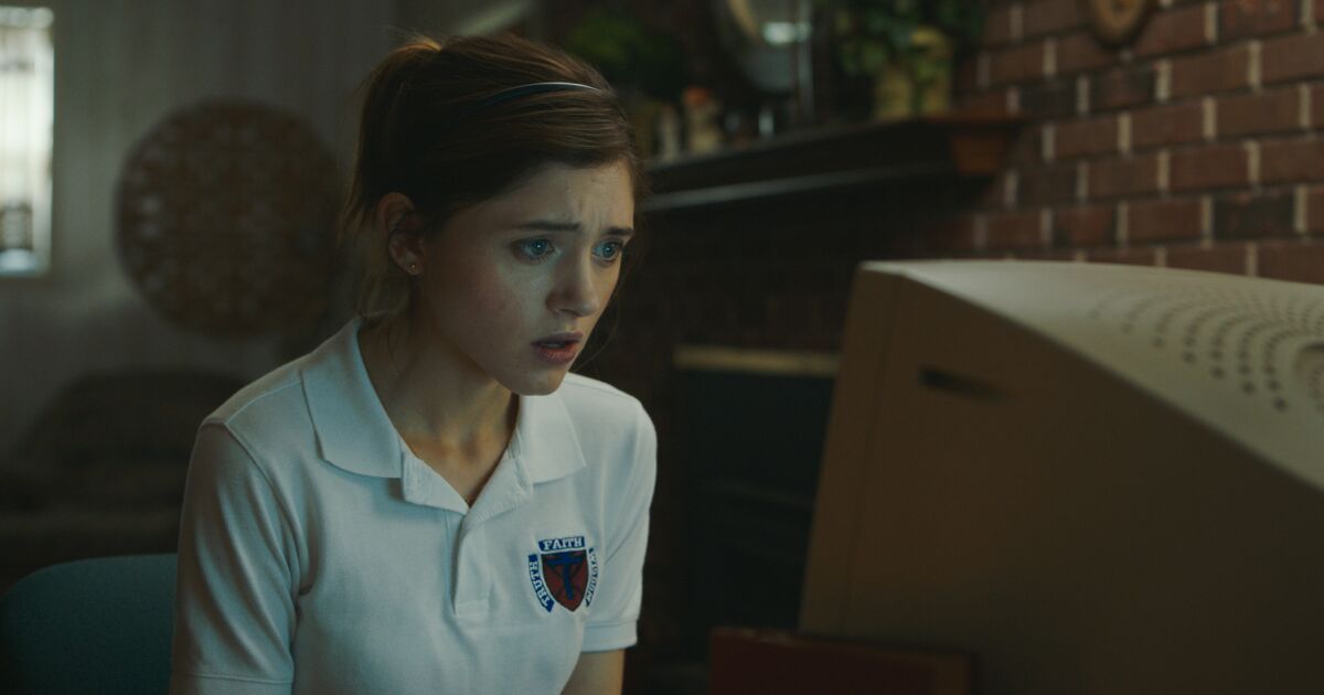 A brunette in a dim lit room, wearing a Catholic school uniform, staring at a computer