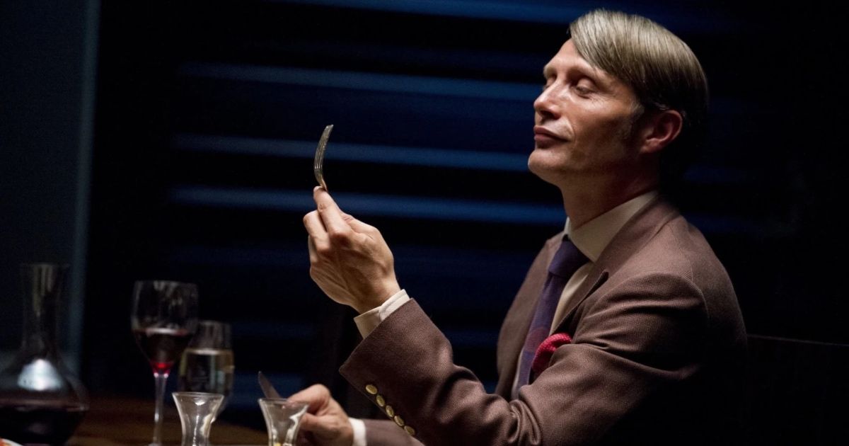 Mads Mikkelsen in Hannibal dressed in a suit and holding a fork