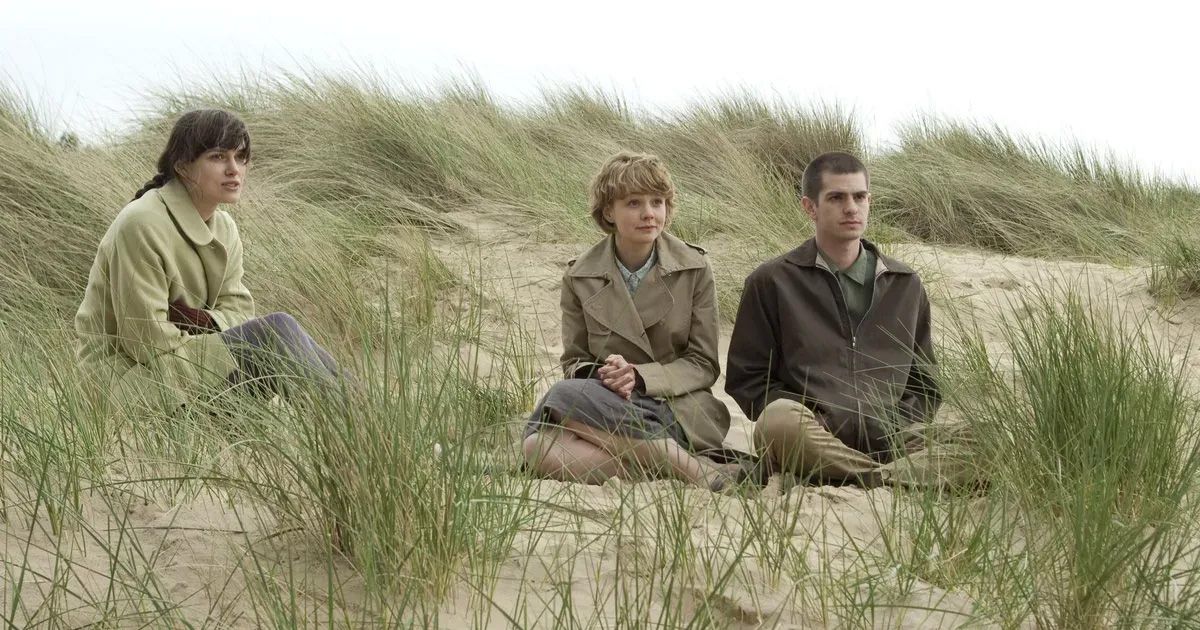 Keira Knightley, Carey Mulligan, and Andrew Garfield sit on a sand dune in Never Let Me Go (2010).