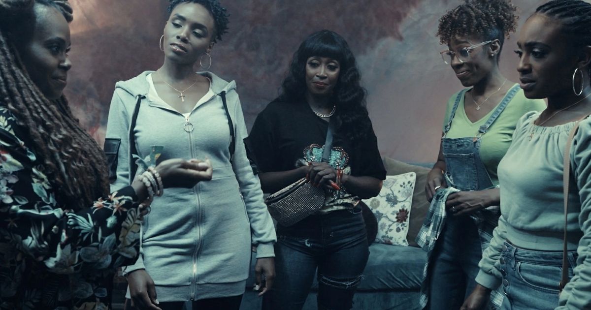The cast of Wicked City, all black women, stand in a circle in a dim lit room