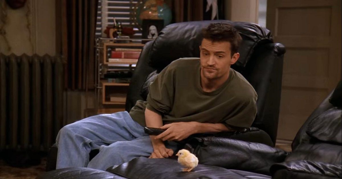 Matthew Perry as Chandler Bing sitting in a chair next to a baby chick in Friends.