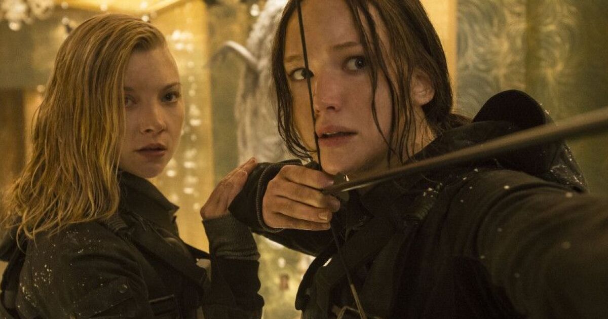 Natalie Dormer as Cressida and Jennifer Lawrence as Katniss Everdeen, as Katniss prepares to shoot an arrow and Cressida holds her arm in The Hunger Games Mockingjay - Part 2