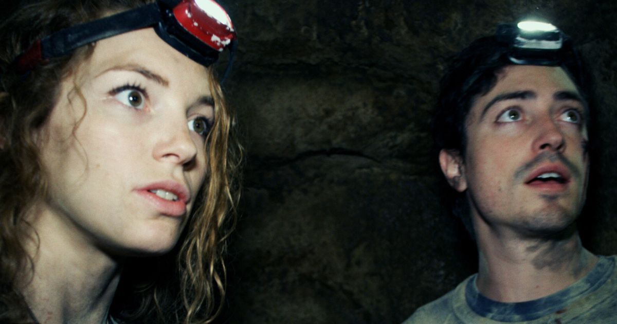 The cast of as above so below underground in a cave with head flashlights on.