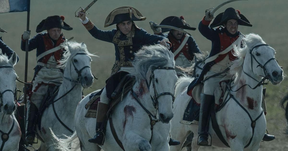 A cavalry of soldiers, including Joaquin Phoenix as Napoleon, ride on white horses, holding their swords above their heads and preparing to attack in Napoleon.