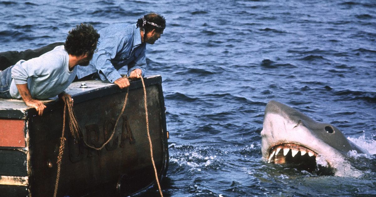 Dois personagens em um barco ao lado de um tubarão em mandíbulas