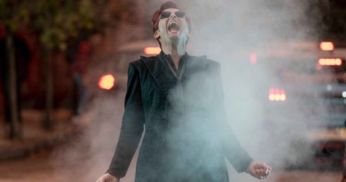 David Tennant como Crowley que está fumando como se estivesse pegando fogo