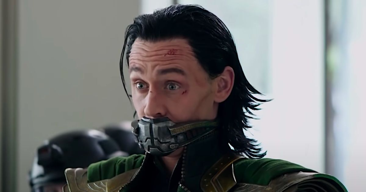 Loki in his green and gold armor and cape, with a device shutting his mouth and cuts all over his face after a battle in Avengers: Endgame.