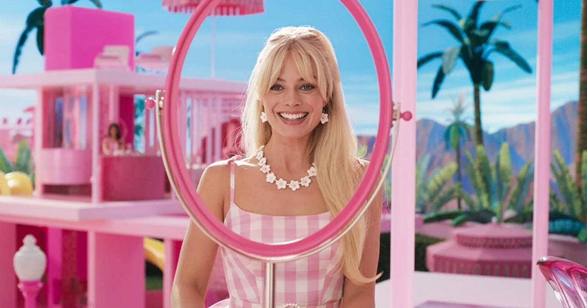 Margot Robbie na Barbie olhando através de um espelho falso na Barbielândia em sua casa rosa com um vestido rosa.