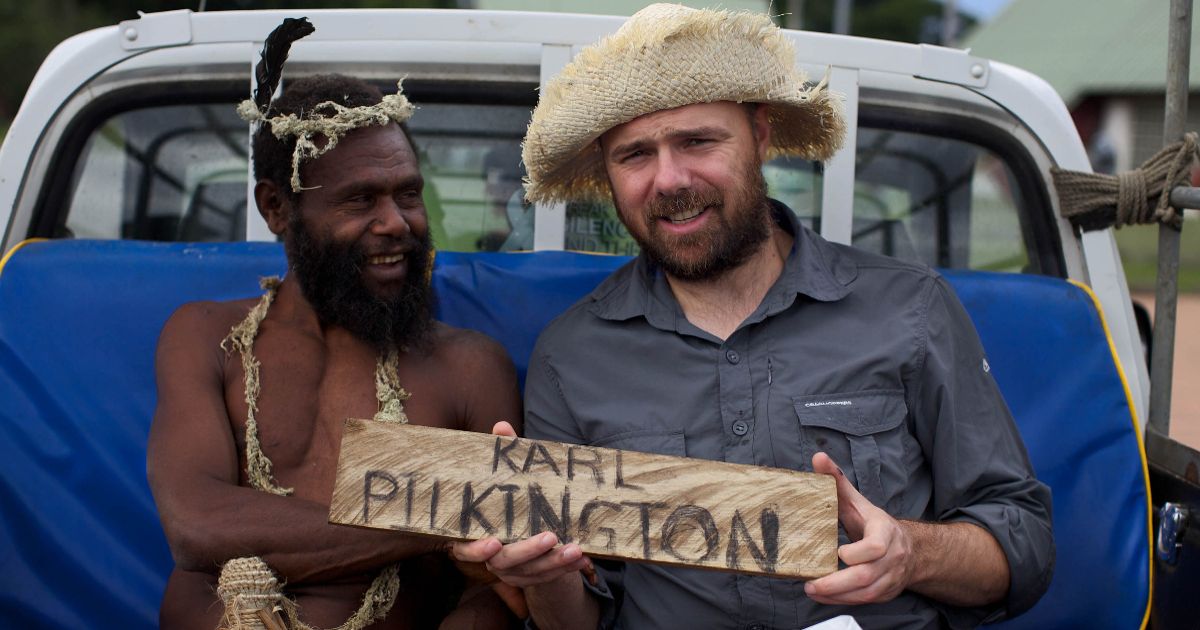 Karl holds a name sign in An Idiot Abroad