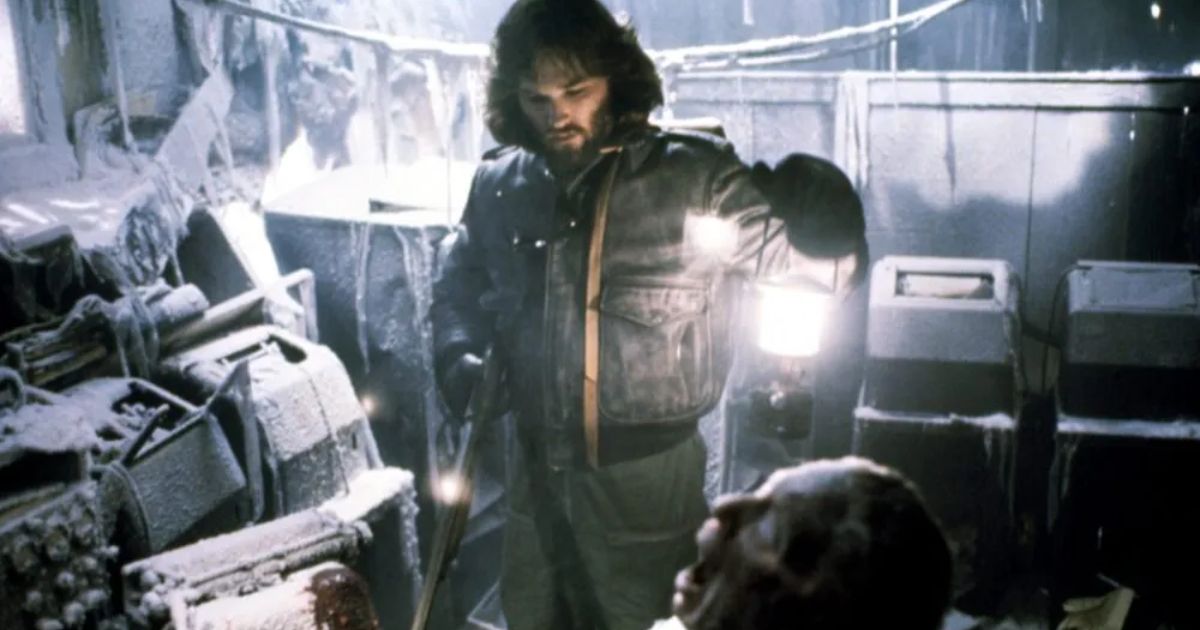Kurt Russell holding a lantern looking at a dead body in The Thing
