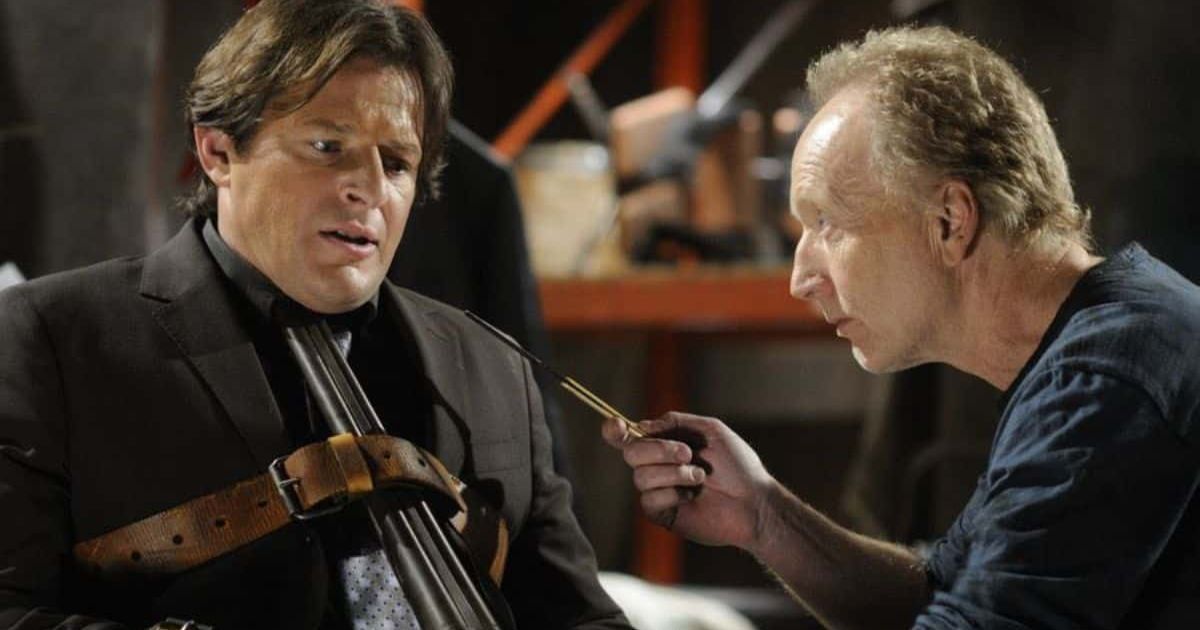 Costas Mandylor as Mark Hoffman in an all-black suit, with a shotgun strapped to his body and neck as Tobin Bell's John Kramer holds something sharp in his hands, pointing it at Hoffman in Saw Costas Mandylor as Mark Hoffman in an all-black suit, with a shotgun strapped to his body and neck as Tobin Bell's John Kramer holds something sharp in his hands, pointing it at Hoffman in Saw Costas Mandylor as Mark Hoffman in an all-black suit, with a shotgun strapped to his body and neck as Tobin Bell's