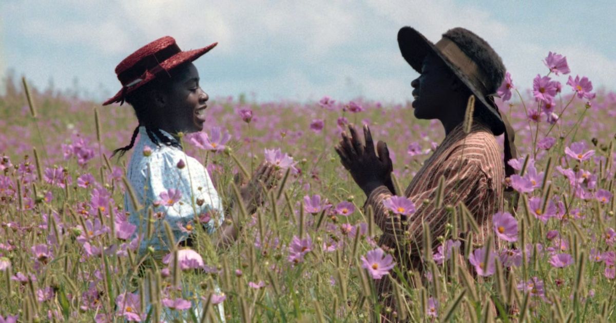 Two women stand in a field with pink flowers in The Color Purple.