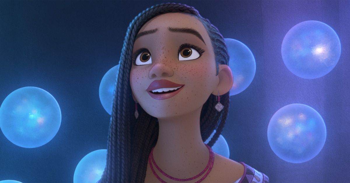 Asha from Wish, played by Ariana DeBose, looking around at magical floating orbs that surround her while wearing a purple dress red necklace, and earrings.