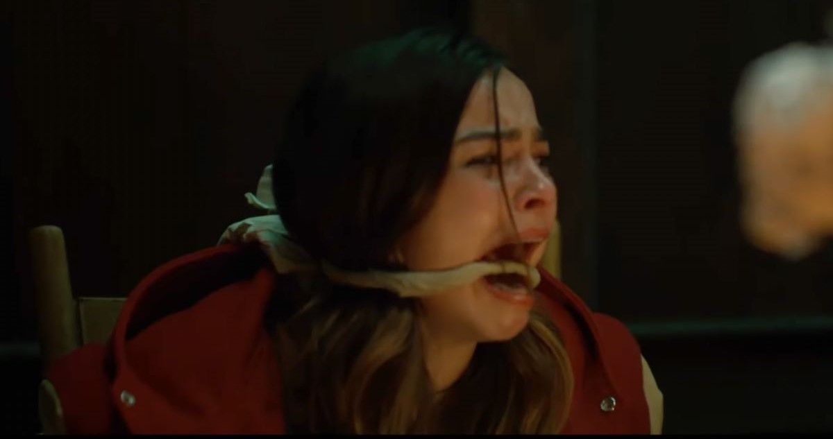 Addison Rae as Gabby wearing a red and cream colored jacket with her mouth being gagged while strapped to a chair in Thanksgiving.