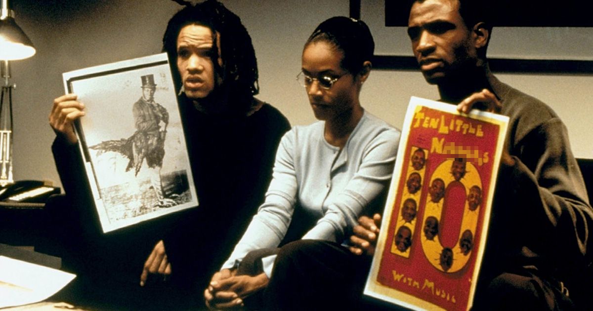 Três personagens de Bamboozled estão sentados em uma sala de reuniões segurando pôsteres racistas de seu programa.