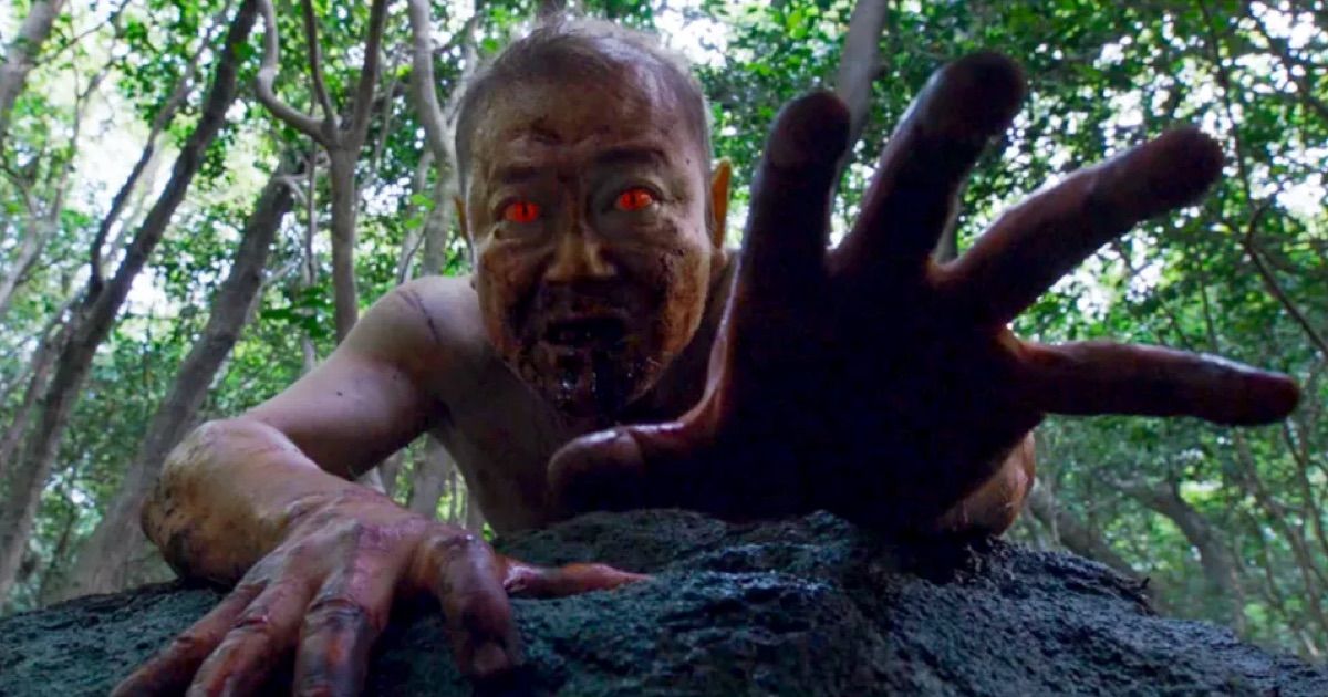 Um japonês com olhos vermelhos brilhantes estende a mão para a câmera na floresta em The Wailing.
