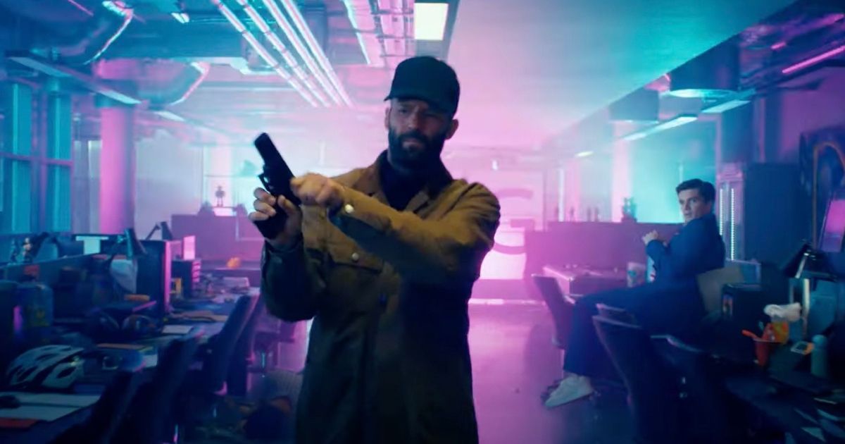 Jason Statham in an office with blue and purple lights, cocking a gun in The Beekeeper