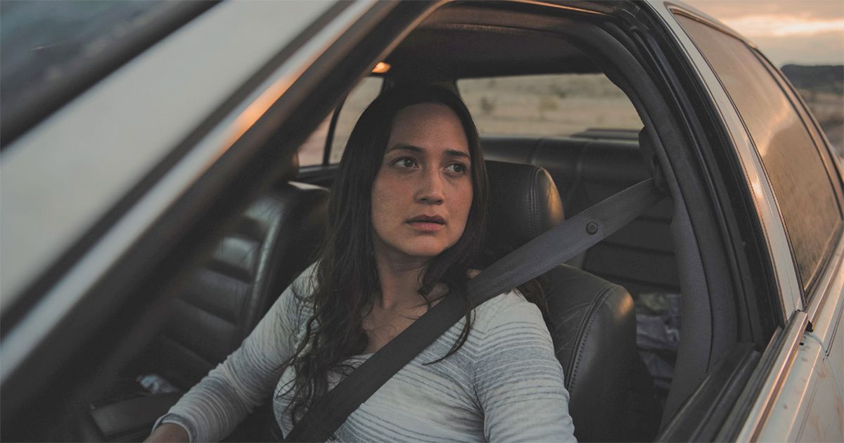 Lily Gladstone no banco da frente de um carro dirigindo em País Desconhecido