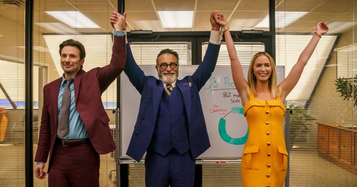 Emily Blunt, Andy Garcia, and Chris Evans hold their hands in the air to celebrate in an office with a whiteboard behind them Pain Hustlers.