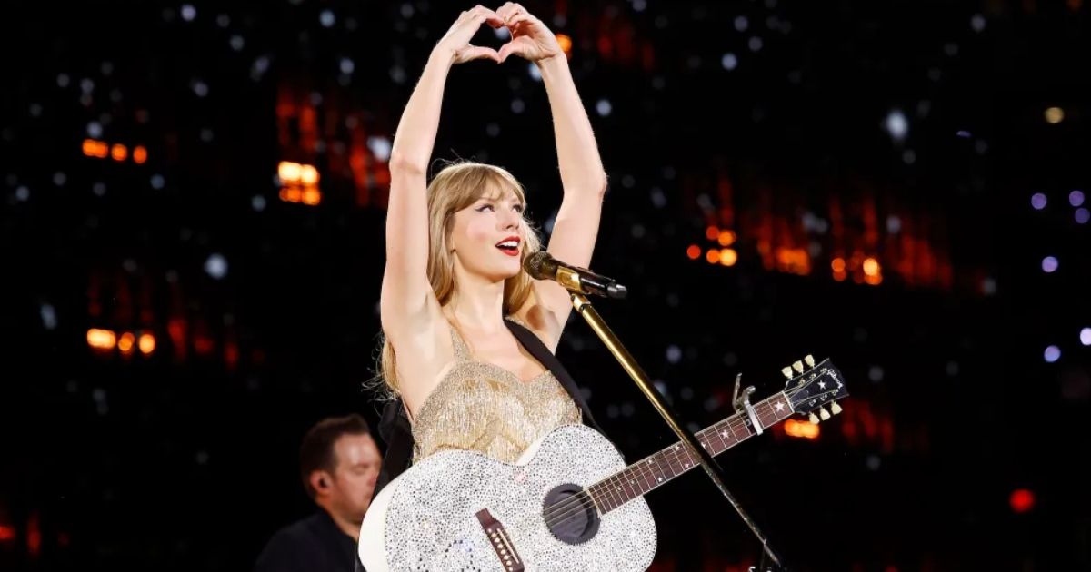 Taylor Swift holding up a heart shape with her hands in the Fearless section of Her Eras Tour movie.
