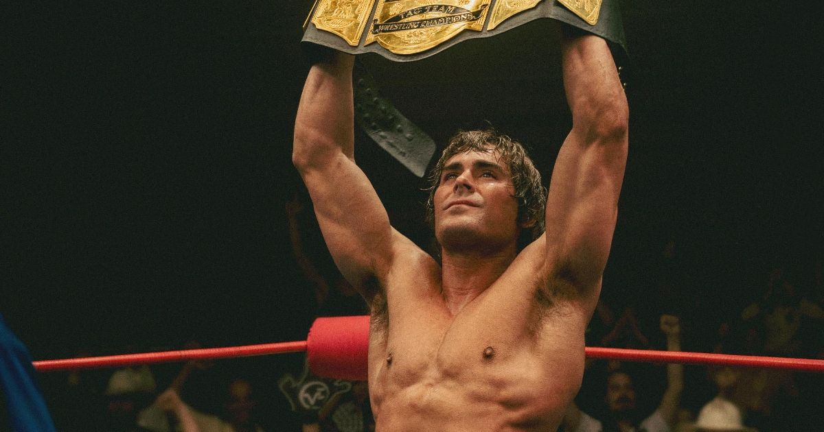 Zac Efron holding up a wrestling championship belt while standing in the ring in The Iron Claw.