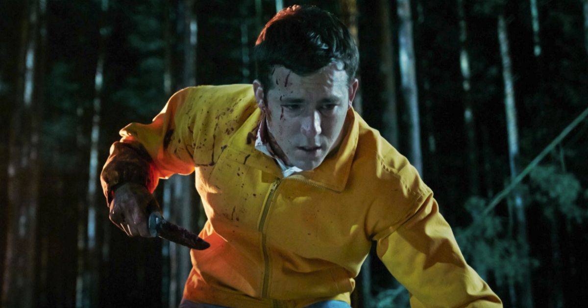 Ryan Reynolds holds a bloody knife with blood on his jacket and face in the woods in The Voices.