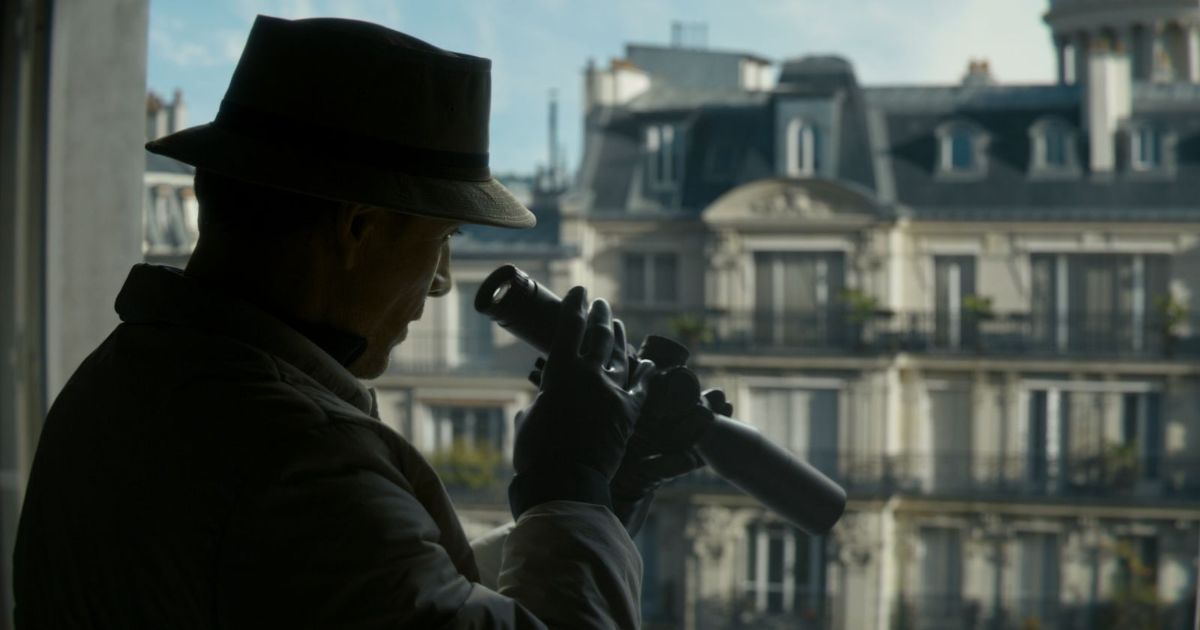 The Killer with Michael Fassbender holding a sniper scope looking at something from a high up balcony.