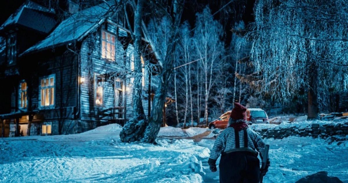 Alguém caminha em direção a uma casa velha na floresta coberta de neve no filme Há Algo no Celeiro