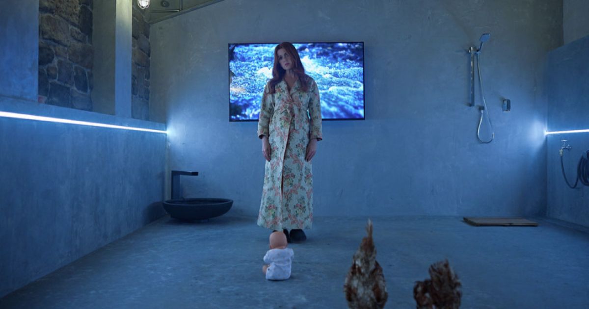 Isla Fisher standing in her basement with a doll and chickens in Wolf Like Me.