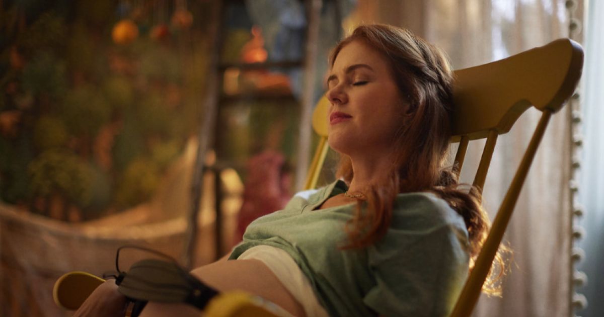 Isla Fisher sitting in a rocking chair while her baby listens to music in Wolf Like Me.