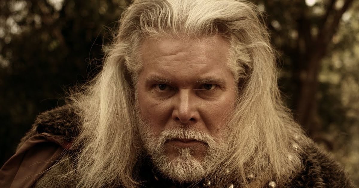Kevin Nash as Odin in Almighty Thor, wearing fur and armor with long grey hair, staring at something off-screen while standing in the forest.