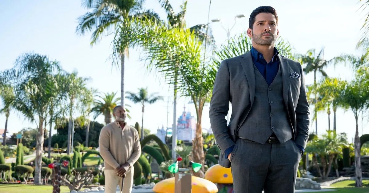 Lucifer wears a gray suit as he stands in a garden filled with palm trees