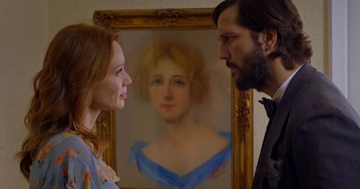 Um homem e uma mulher se entreolham diante de uma pintura de uma mulher idosa.