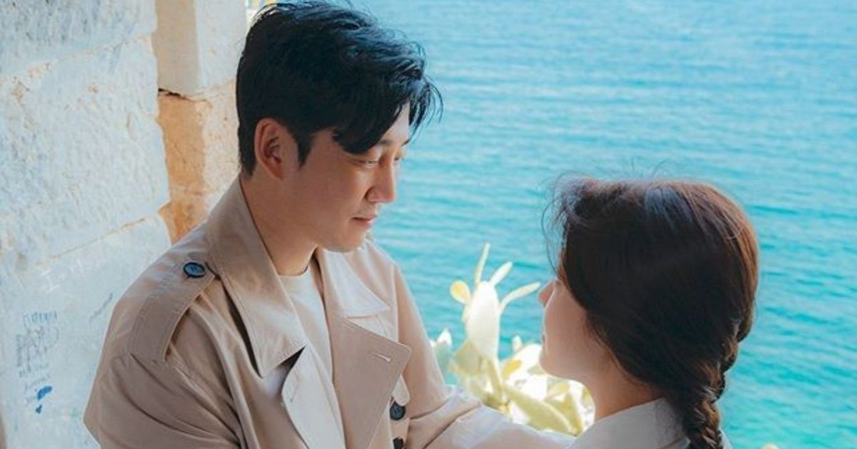 A Korean man and woman stare into each other's eyes, with the ocean in the background.