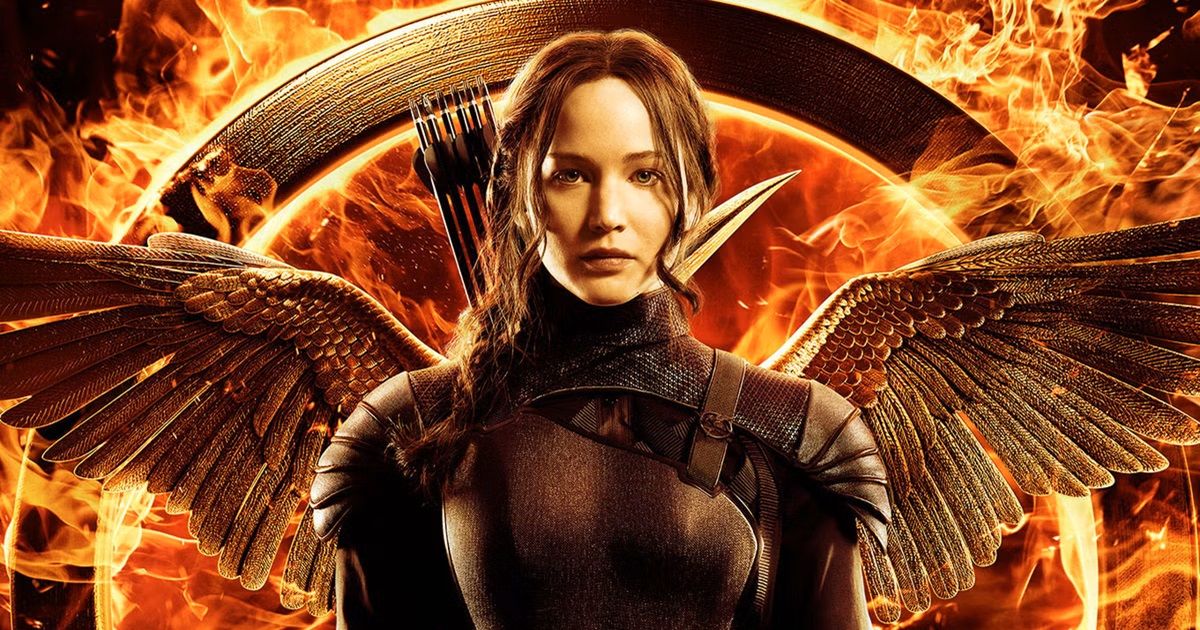 Jennifer Lawrence as Katniss Everdeen wearing black armor with a quiver of arrows behind her as a mockingjay spreads its wings in the background for The Hunger Games: The Mockingjay