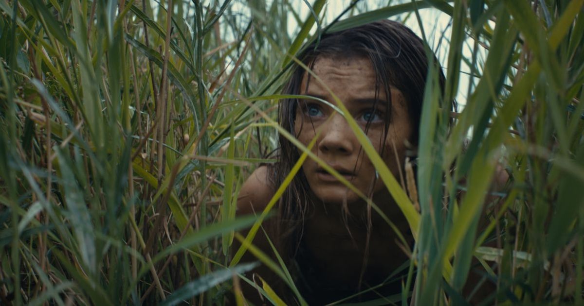 Freya Allan hiding in some large grass in Kingdom of the Planet of the Apes 