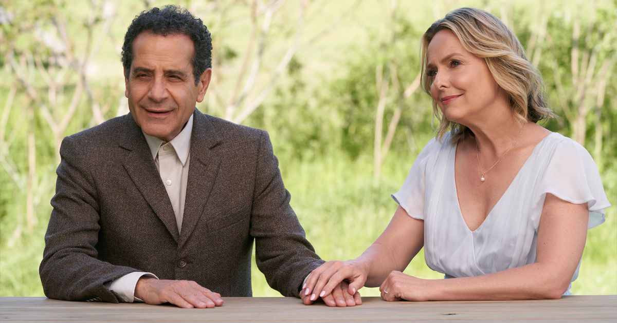 Tony Shalhoub as Adrian Monk, in a suit, and Melora Hardin as Trudy Monk wearing a light colores shirt with a necklace as she holds her hand over Adrian's while they sit at a table outside in Mr. Monk's Last Case: A Monk Movie