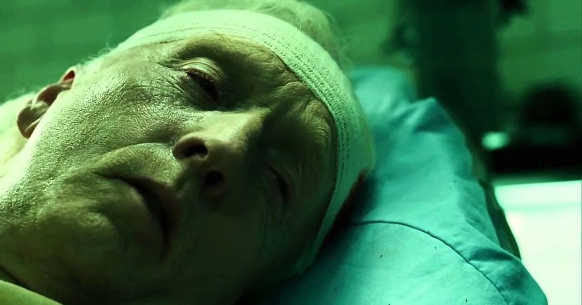 Tobin Bell as John Kramer in a hospital bed with a bandage around his head in Saw III