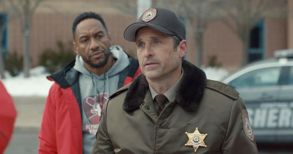 Patrick Dempsey wearing a sheriff's uniform and hat with a man standing behind him in a red coat in Thanksgiving.