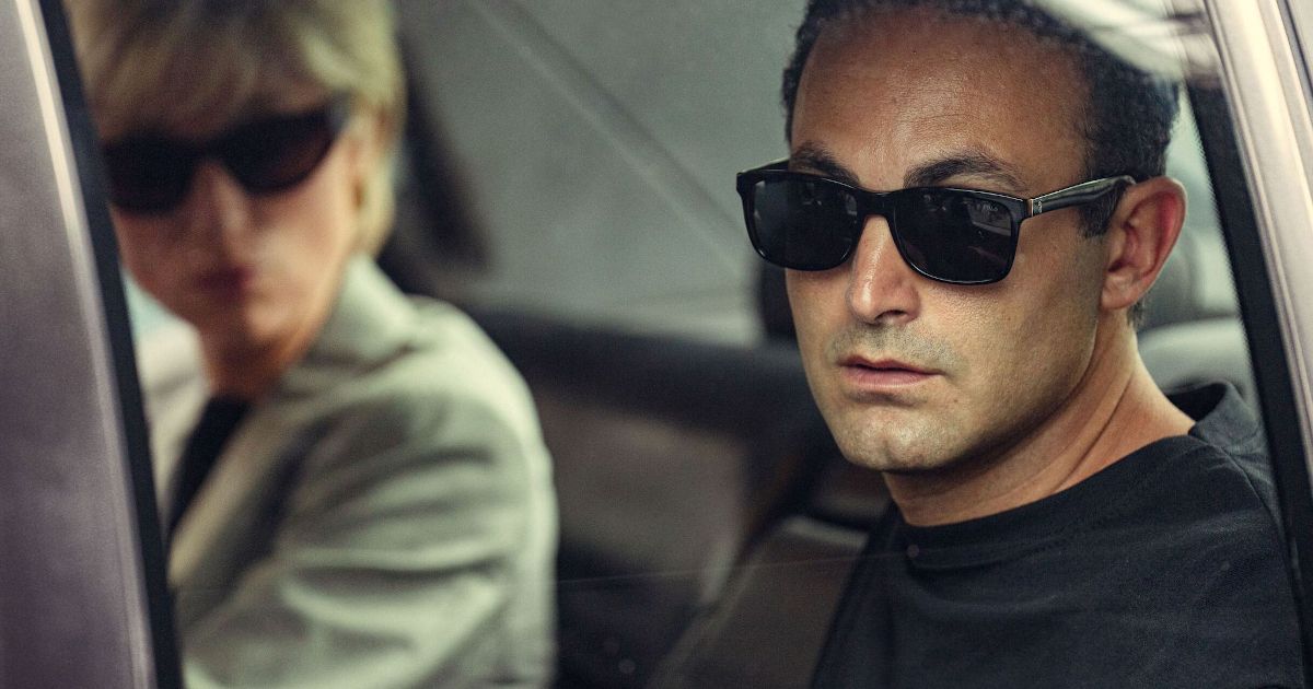 Elizabeth Debicki as Princess Diana and Dodi Fayed in The Crown wearing sunglasses in a car looking out the window.