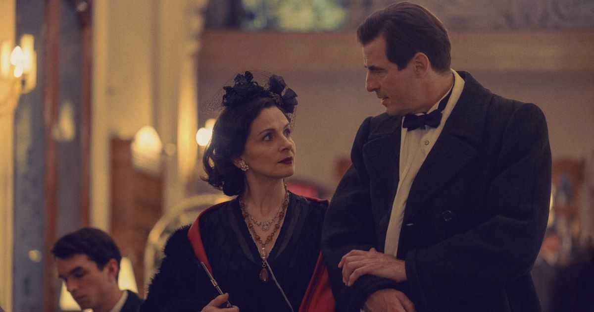Juliette Binoche as Coco Chanel wearing a dark dress and bow with Claes Bang as Spatz walking together in The New Look