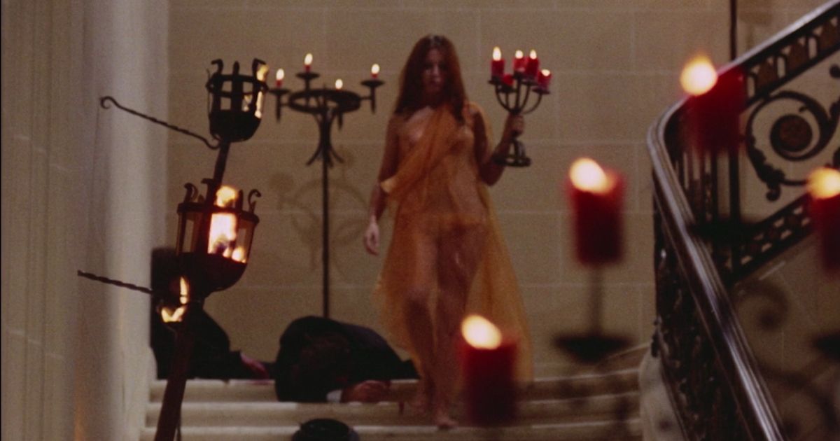 Uma mulher segurando um candelabro desce uma escada iluminada por velas.