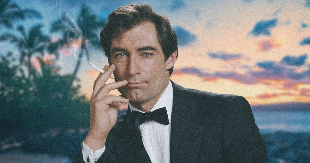 Timothy Dalton as James Bond, smoking a cigarette while wearing a tuxedo on the beach.