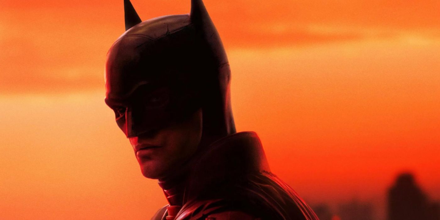 Robert Pattinson as Batman standing in front of an orange sunset in The Batman (2022)