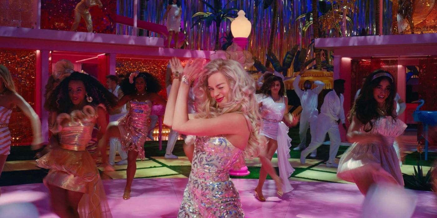 Margot Robbie as Barbie clapping her hands as the other Barbies and Kens dance around her in Barbie (2023).