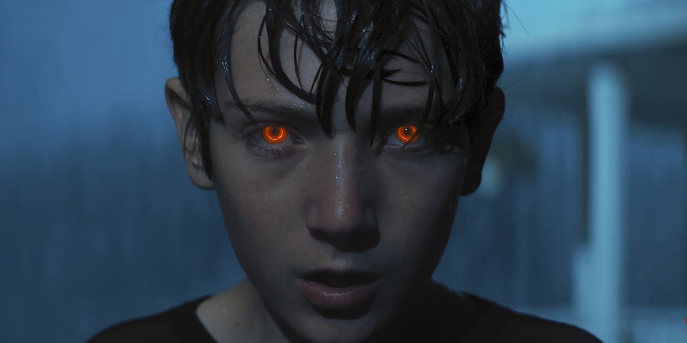 A young man with glowing red eyes is soaked from the rain