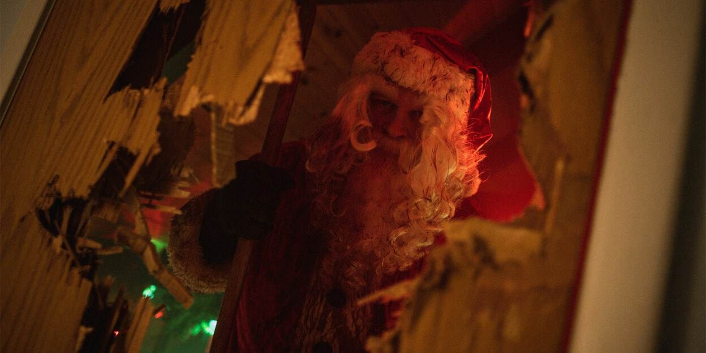 Um andróide vestido de Papai Noel olha através de uma porta quebrada em uma foto do Natal Natal Sangrento