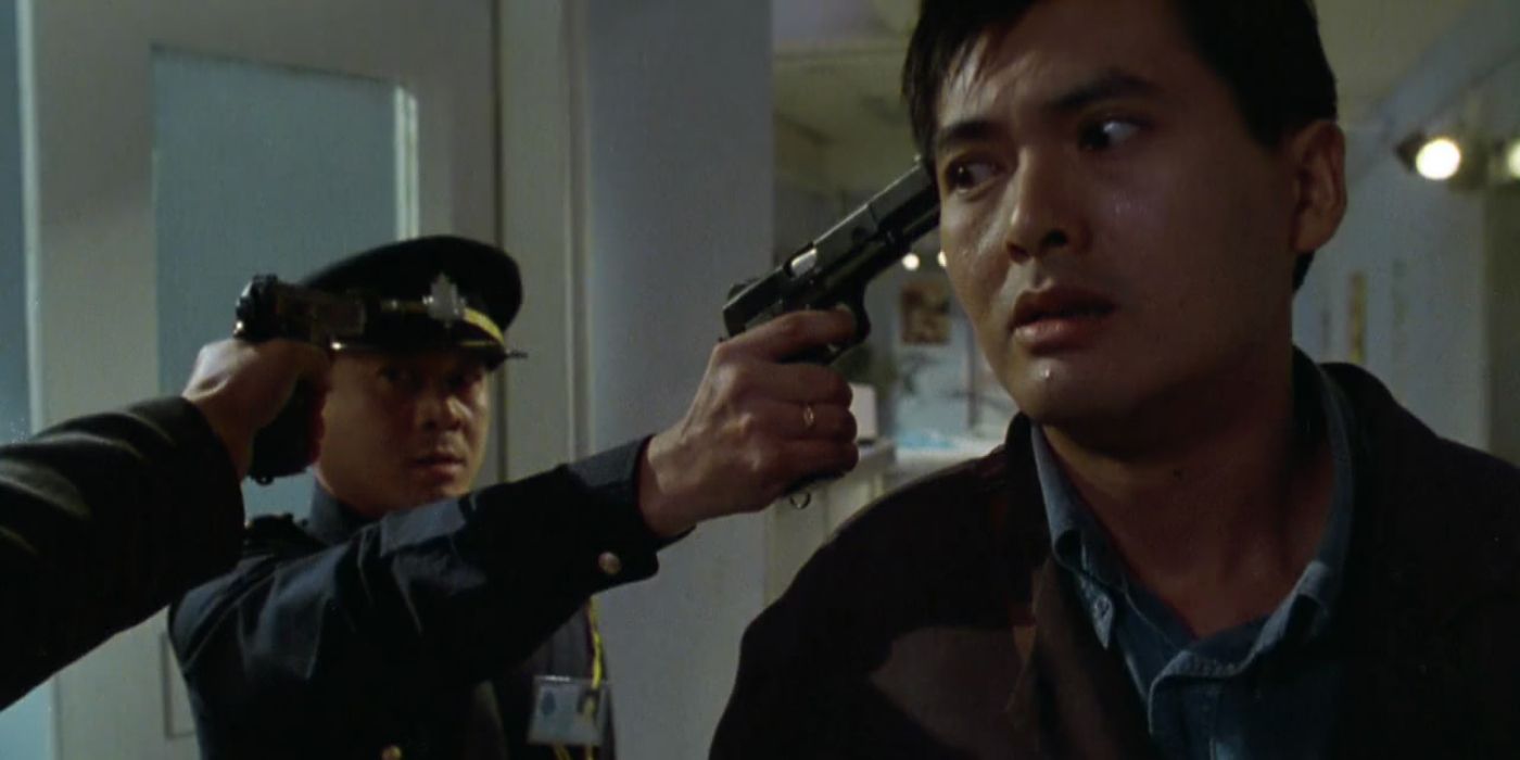 A man out of frame points a gun at a police officer's head, who, in turn, points his gun at Tequila Yuen (played by Chow Yun-fat)